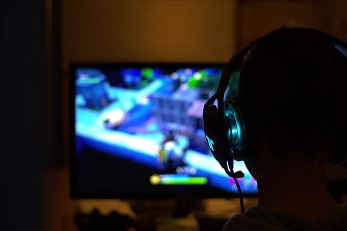 A person wearing headphones plays a video game on a computer monitor in a dark room - Free-Game-Title-Image