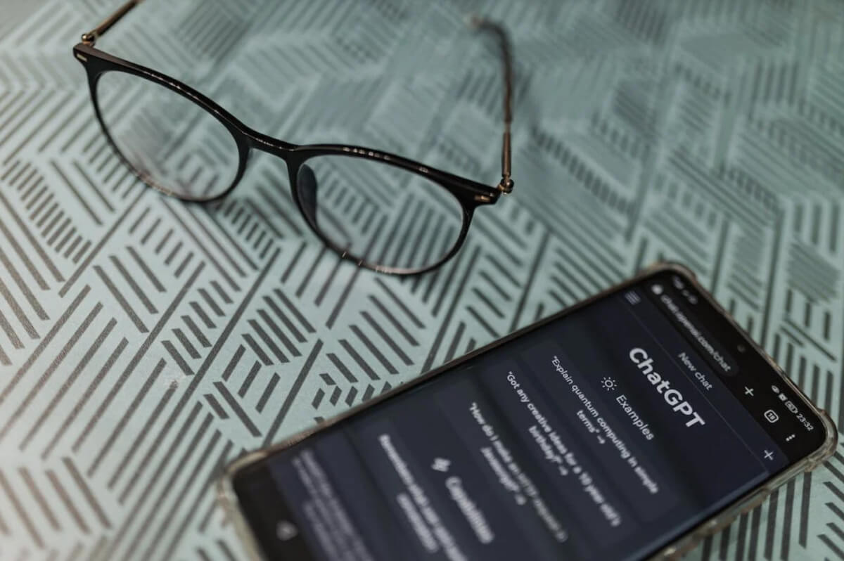 Black-framed eyeglasses rest on a teal surface patterned with thin, parallel lines